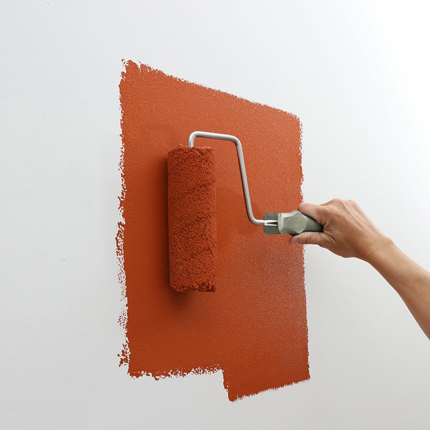 Applicazione di pittura rossa su parete con rullo, per tinteggiatura uniforme fai da te